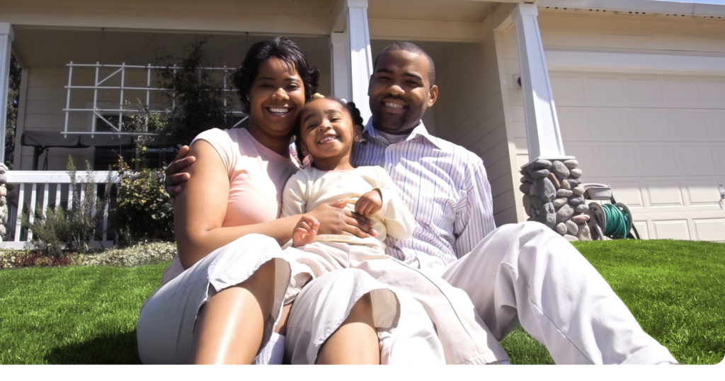 African American family sitting on grass in front of home